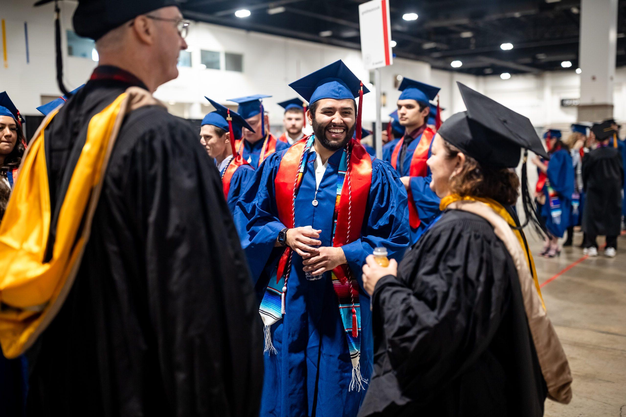 Accounting grad in regalia and laughin while talking to faculty in assembly area of fall '24 commencement